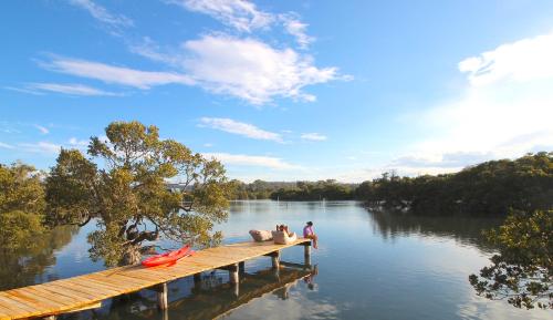 zwei Menschen sitzen auf einem Steg auf einem See in der Unterkunft Batemans Bay Lodge in Batemans Bay