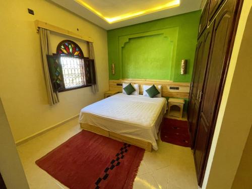 a bedroom with a bed with green walls and a window at Dromadaire Gourmand in Zagora