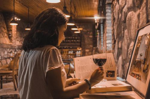 a woman reading a book and holding a glass of wine at Schuchmann Wines Château,Villas & SPA in Tʼelavi