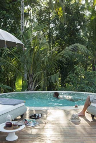 a person sitting in a swimming pool with an umbrella at Sandat Glamping Tents in Ubud