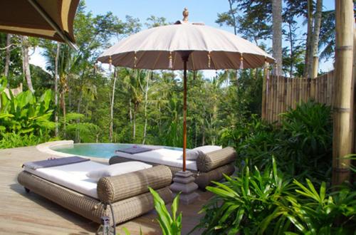 an umbrella and some lounge chairs and a pool at Sandat Glamping Tents in Ubud