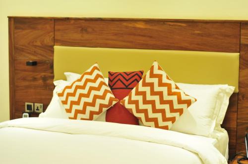 a bed with four pillows on it with a yellow headboard at Millennium Terrace Hotel in Kampala