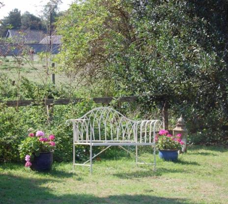 a white bench in a yard with two potted plants at Grange Farm in Thetford