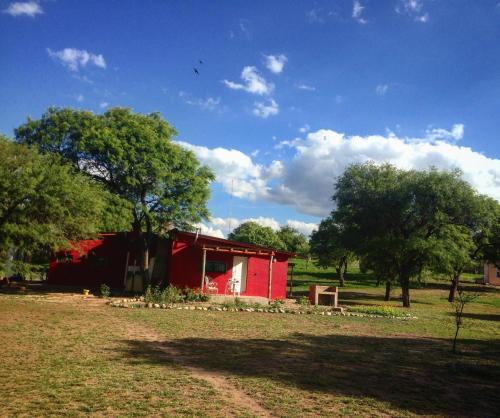 a red barn in a field next to trees at Cabañas Los Algarrobos in San Marcos Sierras