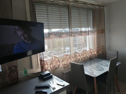 a dining room with a table and a tv and a window at Location d'appartement entièrement meublé près de Genève in Annemasse