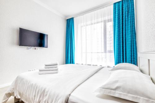 a bedroom with a bed with blue curtains and a tv at RAISSON APARTHOTEL H252 Хан Шатыр in Taldykolʼ