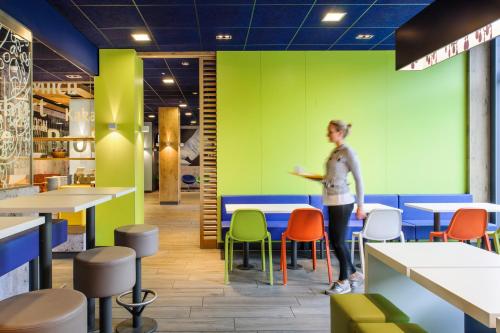 a woman stands in a brightly colored restaurant with tables and chairs at Ibis budget Berlin Potsdamer Platz in Berlin