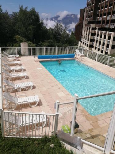 une grande piscine avec des chaises longues et un bâtiment dans l'établissement Les Bergers Alpe d'Huez Pied des pistes et piscine, à Huez