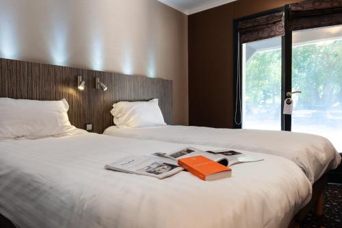 a hotel room with two beds with a book on the bed at Hôtel La Gentilhommière in Nuits-Saint-Georges