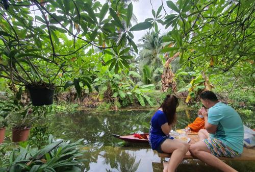 a group of people sitting around a table by a pond at Baan Klong Resort in Damnoen Saduak