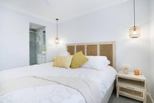 a white bedroom with a large bed and two pendant lights at Entire Residential Home - Lake Illawarra And Beachside Home Sleeps 12 in Lake Illawarra