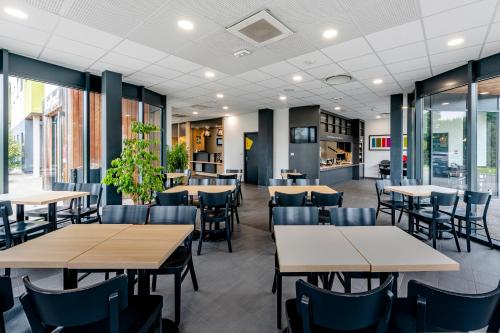 uma sala de jantar com mesas, cadeiras e janelas em B&B HOTEL Bordeaux Est em Tresses