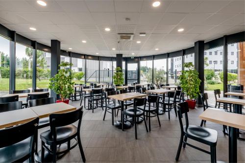 a restaurant with tables and chairs and windows at B&B HOTEL Bordeaux Est 3 étoiles in Tresses