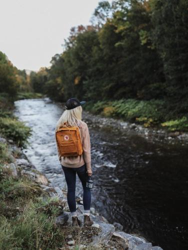 a woman with a backpack standing next to a river at Tälta Lodge, a Bluebird by Lark in Stowe