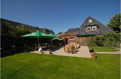 a yard with a house with a green umbrella at Hotel und Restaurant Petit Robby in Wenningstedt