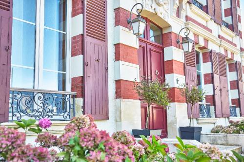 - un bâtiment avec des portes rouges et des fleurs devant dans l'établissement Demeure de Manneville - SPA - 1Km des plages de Cabourg, à Dives-sur-Mer