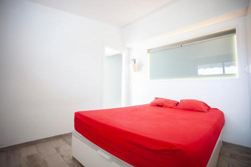 un letto rosso in una camera bianca con finestra di CHALET ADOSADO CON TERRAZA Y AZOTEA a Los Realejos