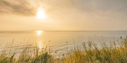 a sunset over a body of water with grass at Ostseehotel Midgard in Damp in Damp