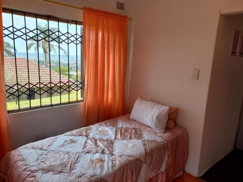 德班的住宿－2 Bedroom Residential Home, along the coast.，一间卧室配有带橙色窗帘的床和窗户