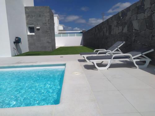 a swimming pool with two chairs and a table at VILLA TRAFALGAR, magnífica casa en la costa ideal para familias que buscan tranquilidad in Playa Blanca