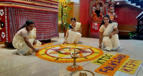 three women kneeling around a rangoli in a temple at KTDC Folk Land, Parassinikadavu in Pāppinisseri