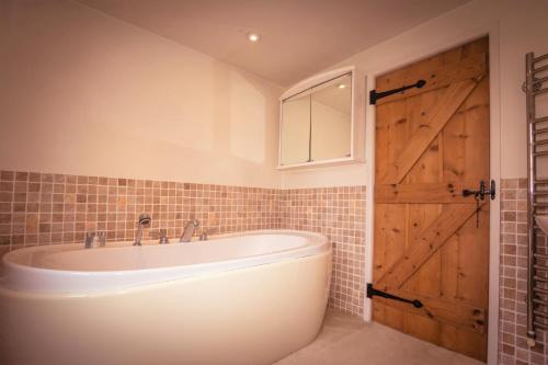 a bathroom with a tub and a wooden door at Pear Tree Cottage in Ratton Village