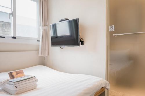 um pequeno quarto com uma cama e uma televisão na parede em Tiin Tinn Inn - Tiehua Xiutai em Taitung City