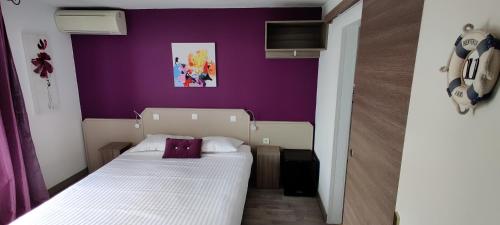 a small bedroom with a purple wall and a bed at Logis Hôtel Les Bleuets in Royan