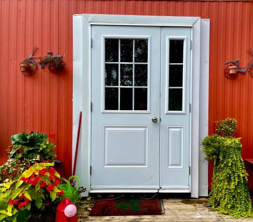 a white door on a red building with flowers at Camping Bomont in Henryville