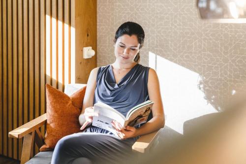 a woman sitting on a bench reading a book at Traumhotel Alpina Superior Adults only Hotel in Gerlos