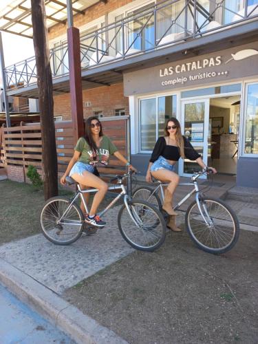 dos mujeres sentadas en bicicletas frente a una tienda en Complejo Turístico Las Catalpas, en Mina Clavero