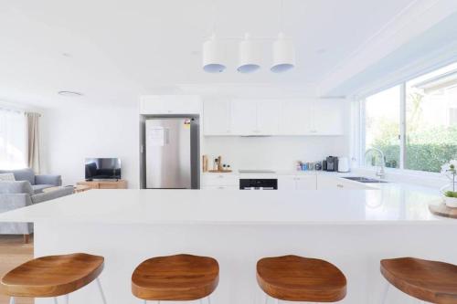 a white kitchen with a white counter and wooden chairs at Abbey House - 3BR/sleeps 8 - South Leura in Leura