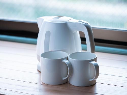 two white coffee pots and mugs sitting on a table at EN HOTEL Hiroshima in Hiroshima