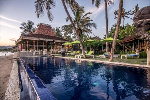 a swimming pool in front of a resort with palm trees at Bali Santi Bungalows in Candidasa