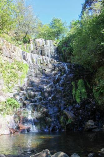 a waterfall on the side of a mountain next to a river at L'AYMERAUDE in Messinhac