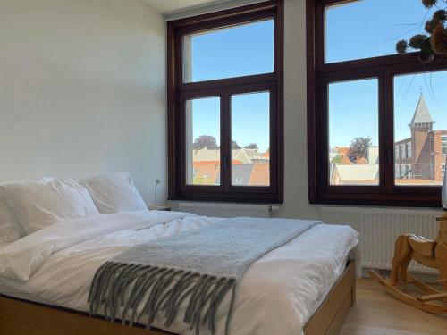 a bed in a room with three windows at Appartement et parking privatif le long de l Escaut in Tournai