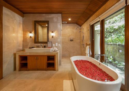 La salle de bains est pourvue d'une baignoire remplie de fleurs rouges. dans l'établissement The Allure Ubud Villas, à Ubud