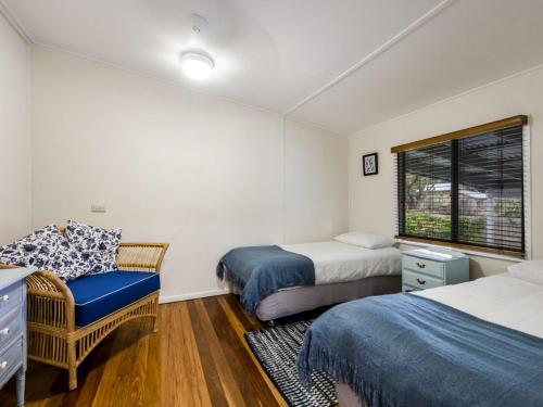 a bedroom with two beds and a chair and a window at Salt Water Cottage in Iluka