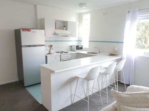 a white kitchen with a white refrigerator and stools at Royal Park Retreat in Melbourne