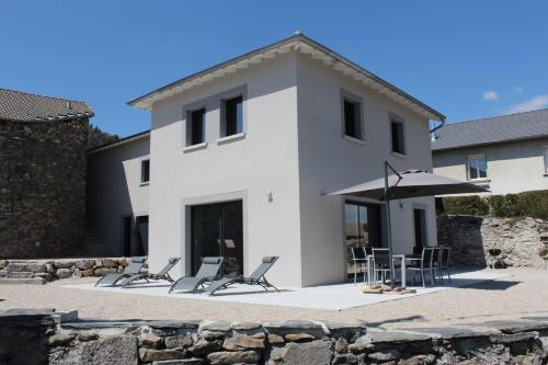 a white house with chairs and an umbrella at L'AYMERAUDE in Messinhac