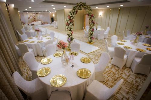 a banquet hall with white tables and white chairs at Sama Muscat Hotel in Al Khawḑ