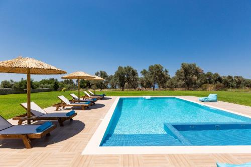 a swimming pool with chairs and umbrellas next to a field at Villa Litinas in Kiriánna