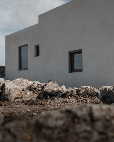 a white building with windows and rocks in front of it at Santorini Sky, The Lodge in Pirgos
