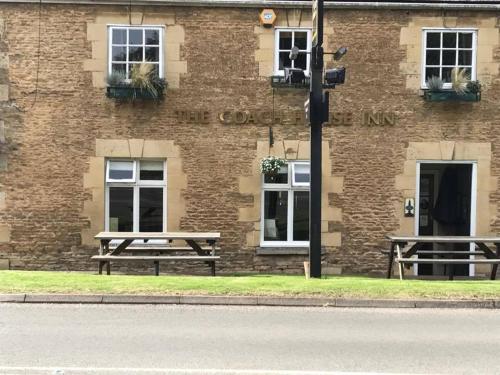 un edificio de ladrillo con dos mesas de picnic delante de él en The Coach House Inn en Oakham