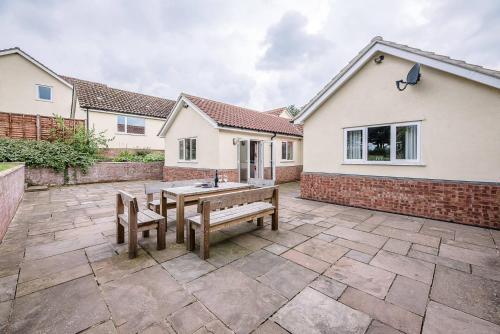 a patio with two benches in front of a house at Grove Farm Bungalow with swimming pool, Dallinghoo in Woodbridge