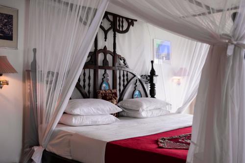a bedroom with a canopy bed with white sheets and pillows at Tembo House Hotel in Zanzibar City