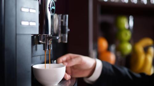 a person is holding a cup in a coffee machine at Intercontinental Shenzhen Dameisha Resort by IHG in Shenzhen