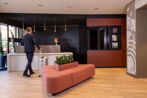 a man walking through a lobby with a orange couch at Hotel La Diligence in Obernai
