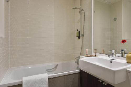 y baño con bañera blanca, lavabo y ducha. en Citadines Montparnasse Paris en París