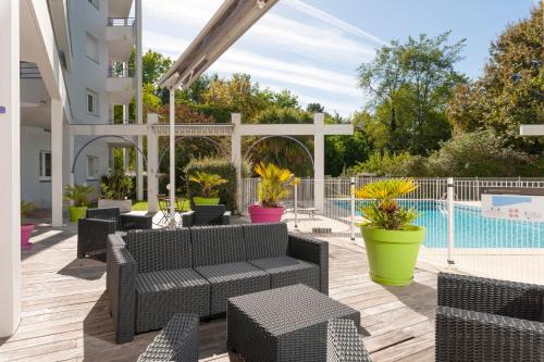 a patio with black wicker furniture and a pool at CERISE Dax - Les Jardins du Lac in Saint-Paul-lès-Dax